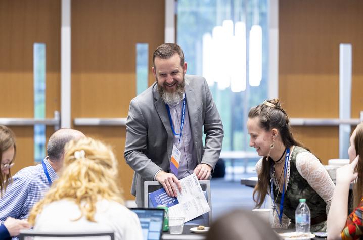 Professor standing over five sitting conference participants while speaking with them
