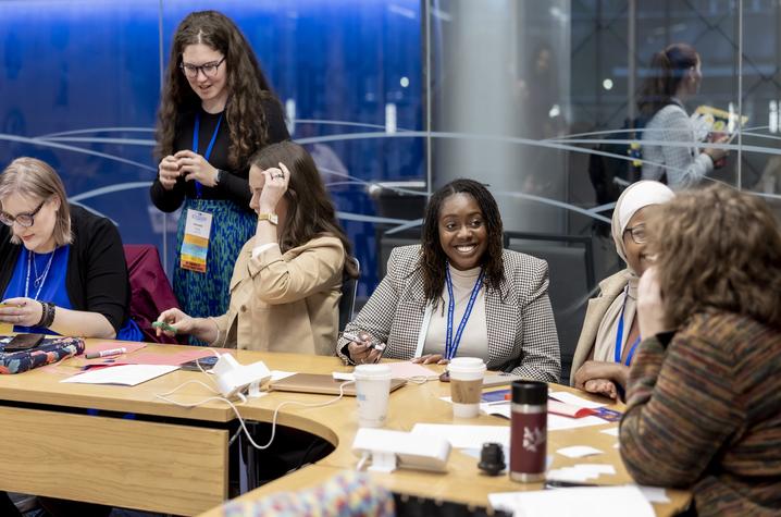 Five people sitting around a conference table with one person standing in the background 