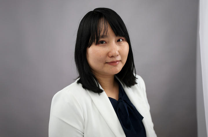 Photo of Khine Zin Aung A professional portrait of a woman with shoulder-length dark hair wearing a white blazer and dark blouse, looking toward the camera against a gray background.