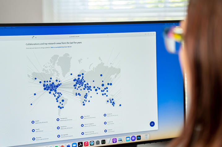 Woman looks at Scholars at UK portal on computer screen with world map