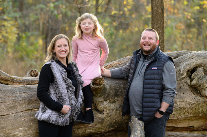 image of Sarah Beth sitting on log with her parents
