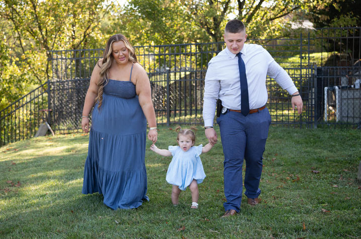 Photo of Hillerman family Two parents holding the hand of their young daughter