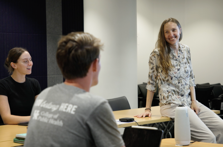 A person is sitting on a table speaking to two others during a classroom or meeting discussion.