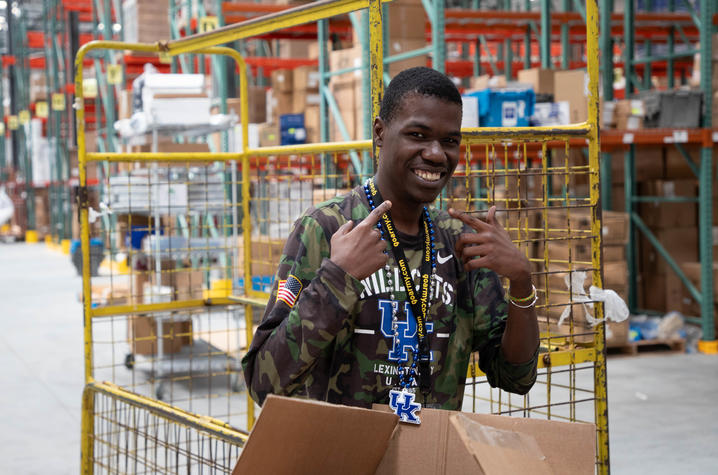 A student with Project SEARCH is in a warehouse smiling after helping move materials around with carts and pallet lifts.