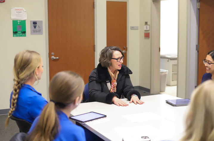 A small group of health profession students sit around a table listening as an instructor speaks during a classroom discussion.