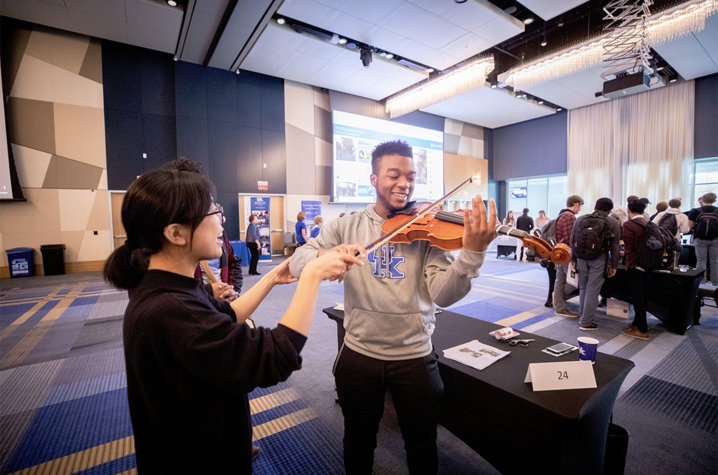 Student holding violin (right) with assistance from expert (left)