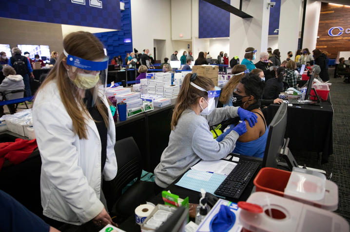 photo of several people in UK vaccination clinic including one woman getting a shot.