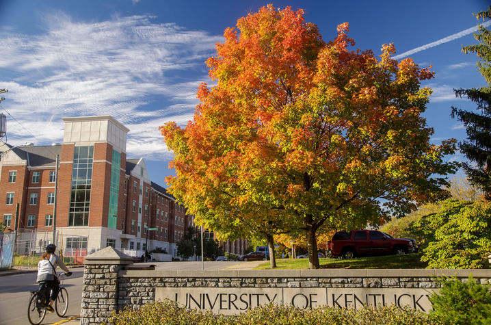 Fall foliage frames the University of Kentucky sign as a cyclist passes by on campus.