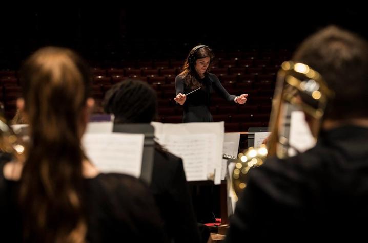 photo of Kaitlin Bove (in headphones) conducting UK Concert Band in 2018