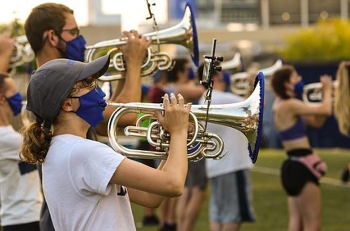 photo of masked members of the Wildcat Marching Band playing horns with covers on the bells