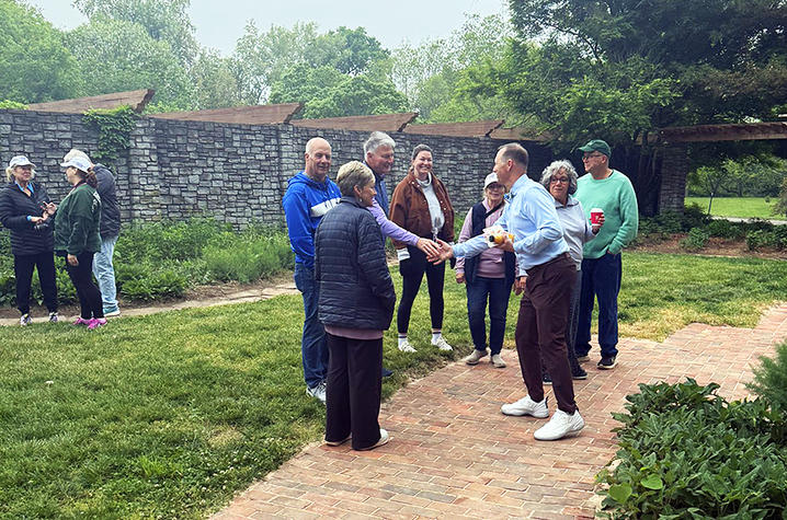 Participants gather along a brick path outdoors. There is a stone wall in the background.