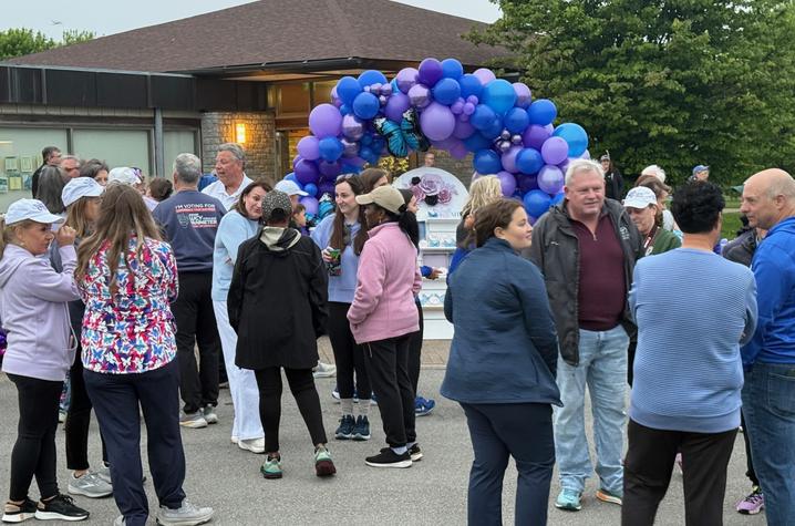 Participants gather beneath a purple-and-blue balloon arch in an outdoor setting.