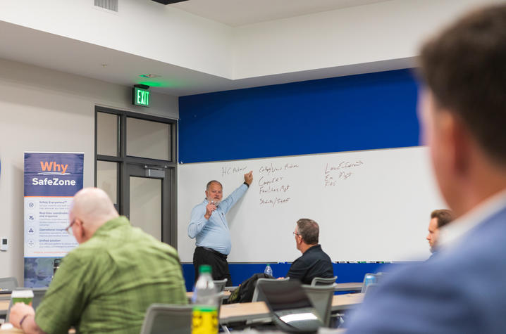 Chief Monroe gestures toward a whiteboard while leading a discussion during a campus safety session, with participants seated and a “Why SafeZone” banner displayed in the room.