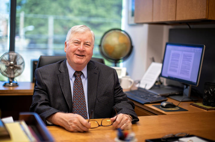 Richard Ausness seated at desk in suit holding glasses