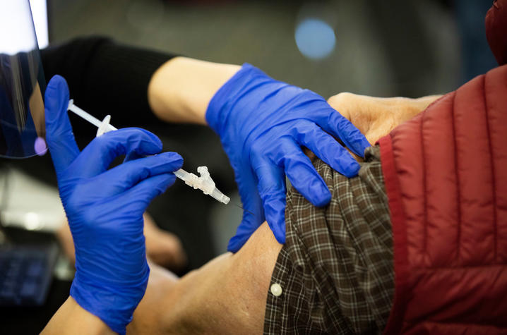gloved hands getting ready to put needle with covid vaccine in a man's arm