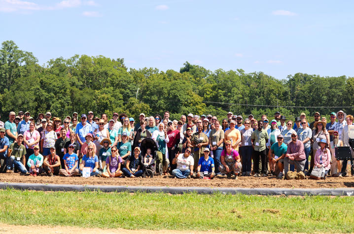 2026 Appropriate Tools & Technologies Field Day Attendees A large group of field day participants gathers for a group photo in a cultivated agricultural plot. Attendees stand and kneel in several rows across the width of the field, with some wearing hats, sunglasses, and name badges.