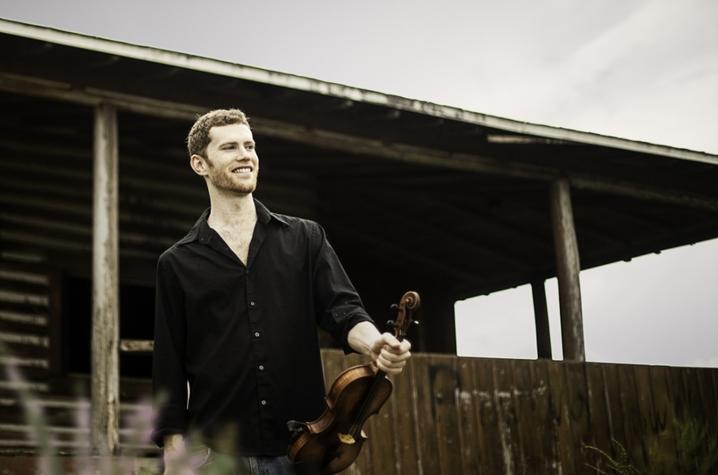 photo of Andrew Finn Magill outside cabin holding fiddle