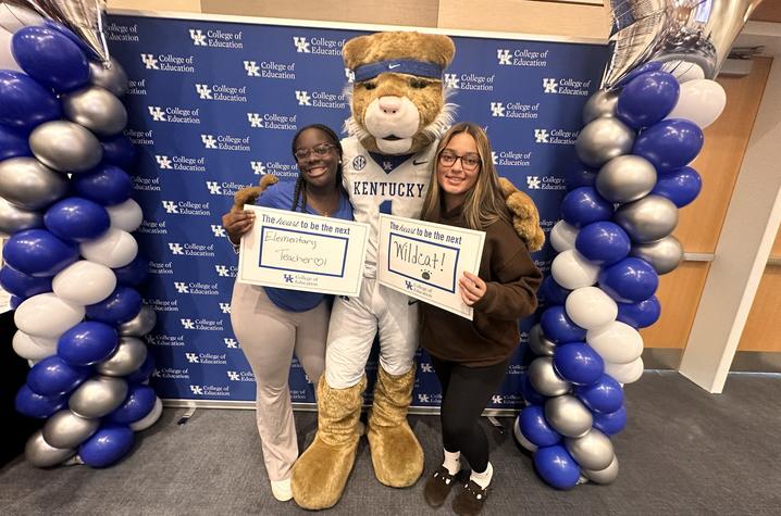 photo of Wildcat with future teachers Two people pose with the UK Wildcat mascot in front of a College of Education backdrop, framed by blue, white and silver balloons. They hold signs reading “The heart to be the next Elementary Teacher” and “The heart to be the next Wildcat.”
