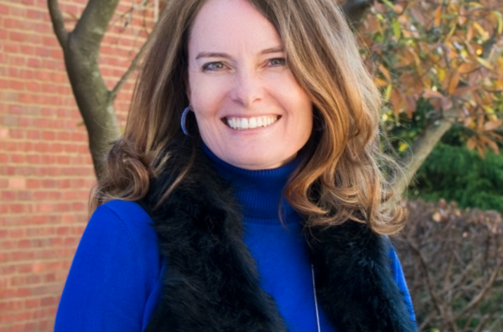  Erin N. Haynes, DrPH, MS, pictured in front of a brick building and tree with fall leaves. She wears a blue turtle neck and a black vest. Her light brown hair is shoulder length and she's smiling at the camera. 