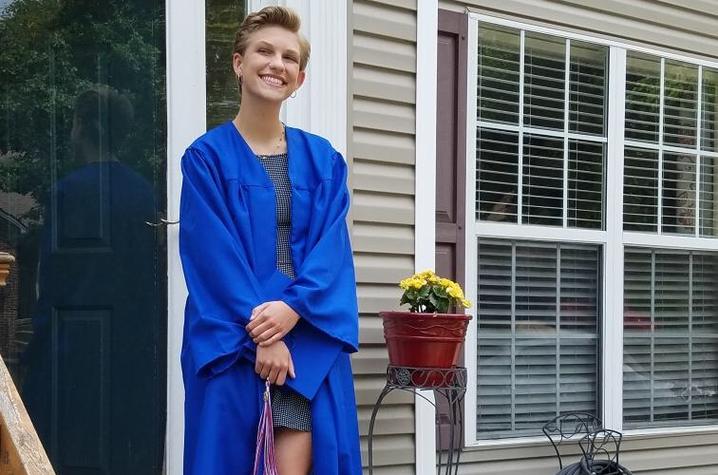 photo of Grace Cruse in graduation gown outside door to a home with mortar board in hand