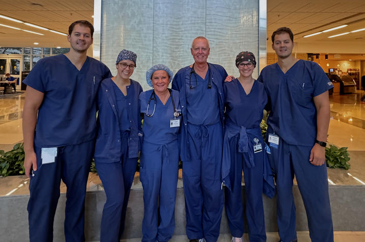 Six people in medical scrubs standing together indoors, smiling at the camera.