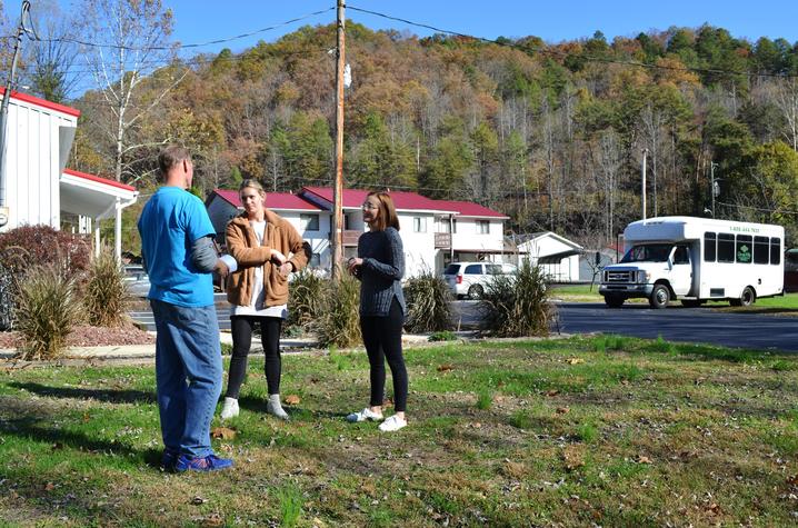 Three individuals in discussion outdoors near tree-topped hill