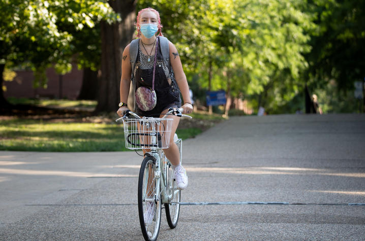 female student wearing mask bicycling on campus during covid pandemic