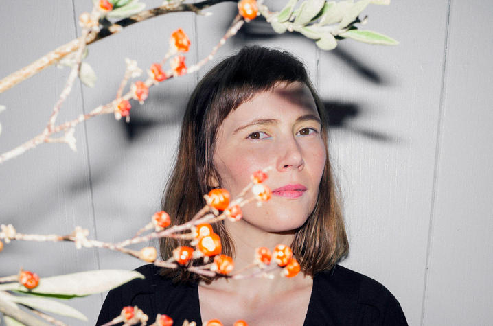 Branches with small orange berries in front of a person wearing a black top against a light-colored wall.
