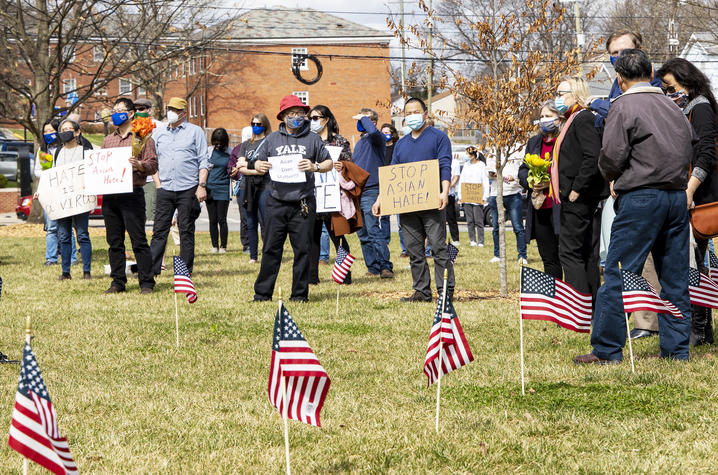 Rally attendees holding signs in front of American flags on lawn in front of Memorial Hall.