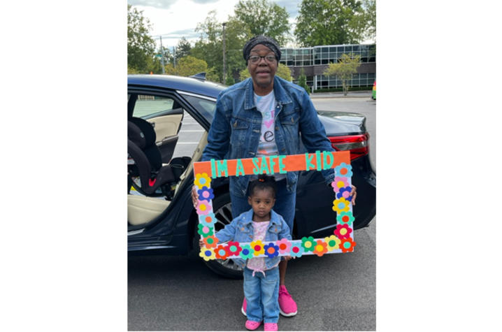 image of woman and young girl holding a sign that says "I'm a safe kid" at car seat inspection event