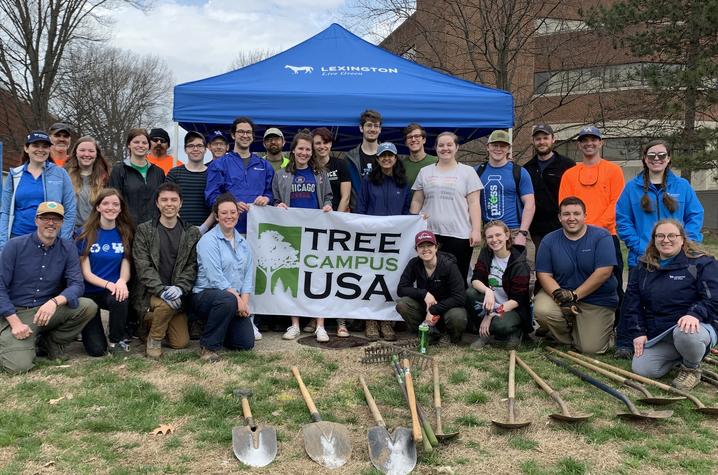 photo of group of people prior to a tree planting and a sign that says Tree Campus USA.