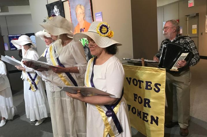 photo of 4 members of Women’s Suffragist Centennial Chorus backed by man on accordian