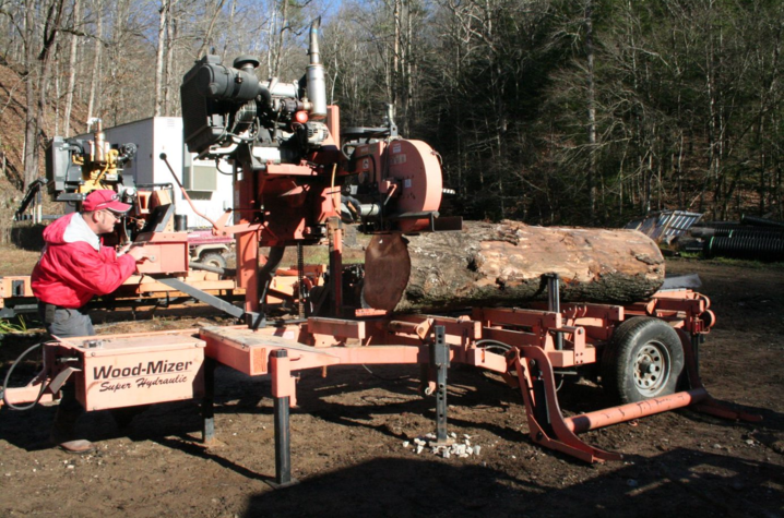 Doran Howard, wearing red jacket and ballcap, saws timber into slabs.