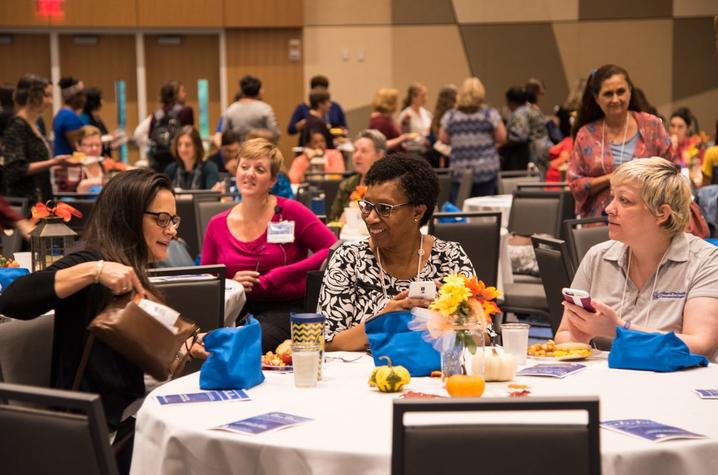 Women attending conference sitting at round table in ballroom engaged in conversation