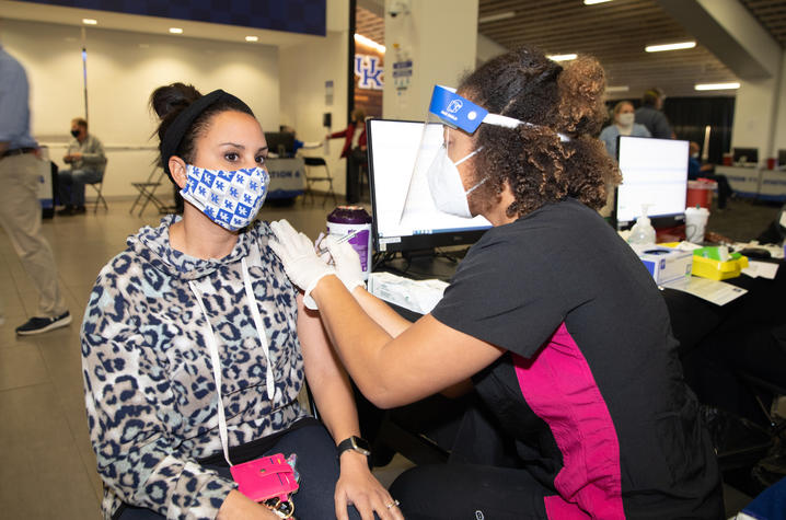 woman receives covid shot in her left arm at UK vaccination clinic