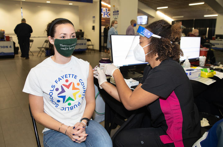 Teacher with Fayette County Public Schools T-shirt receives COVID-19 vaccine shot at Kroger Field vaccination clinic.