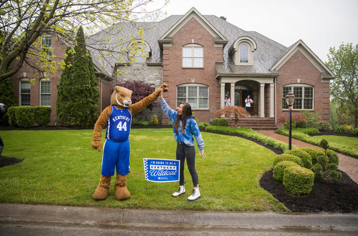Wildcat high fives with incoming freshman in her front yard with yard sign saying "I'm going to be a Kentucky Wildcat"