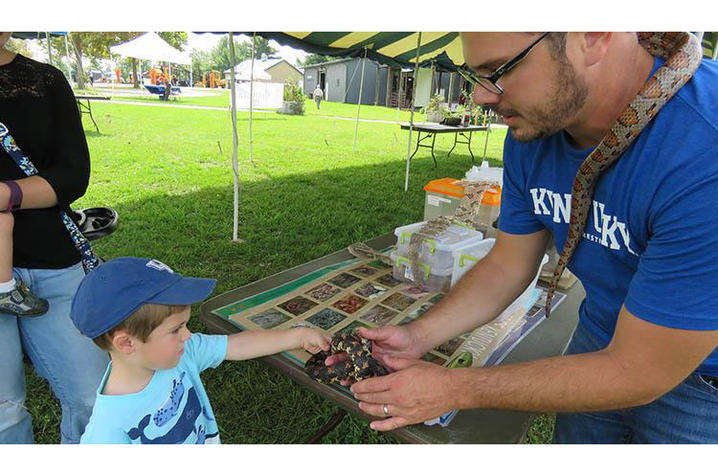 Man with snake presenting it to little boy in ballcap to pet