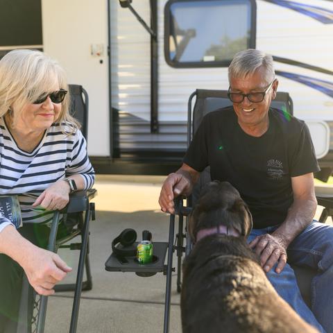 Photo of woman and man petting a dog while sitting in front of an RV