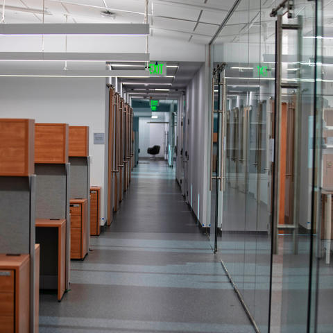 A dimly lit hallway with cubicles to one side and glass walled offices to the other.