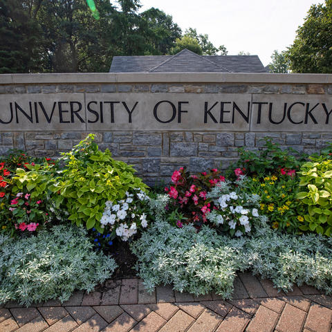 photo of stone wall at campus entrance that says "University of Kentucky" and has blooming flowers in front of it