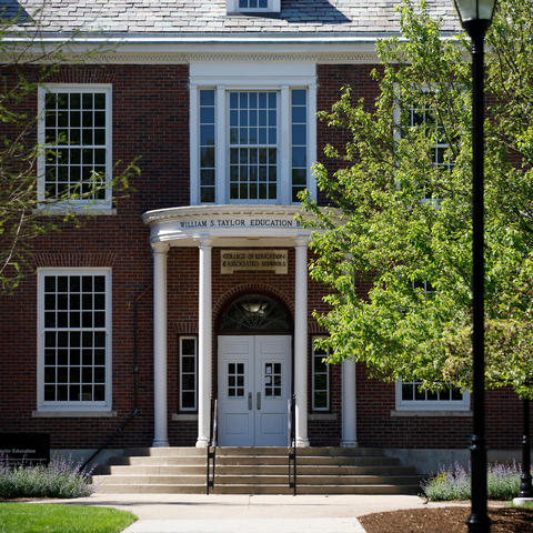 This is a front-view photo of the UK Taylor Education Building with trees and grass in sunlight in the foreground.