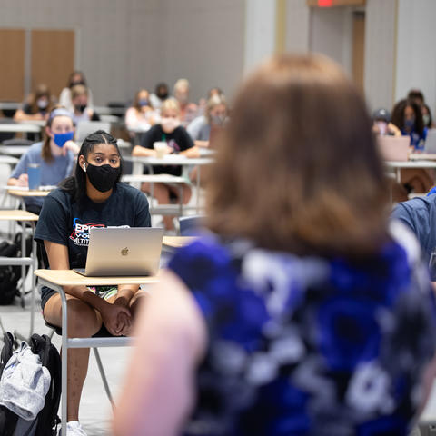 photo of journalism class with students in  masks and back of College of Communication and Information Dean Jennifer Greer's head as she speaks to them.