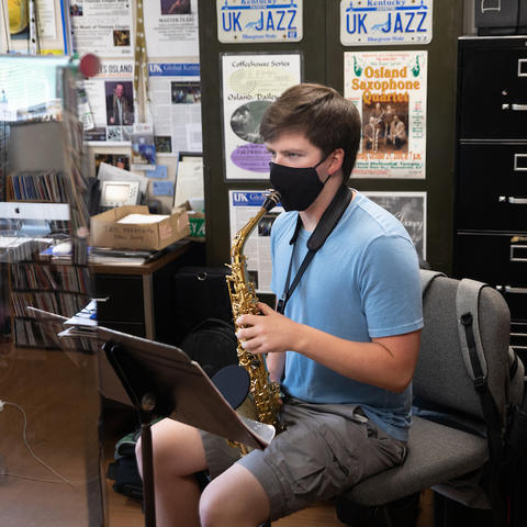 photo of masked saxophone student taking lesson in Miles Osland's office behind plexiglass
