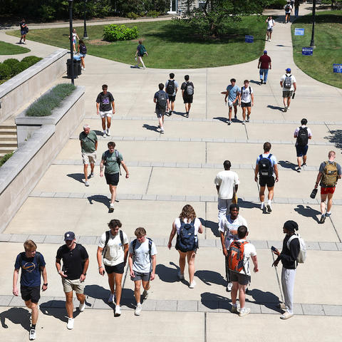 groups of students walking outside on a sidewalk, seen from an elevated viewpoint