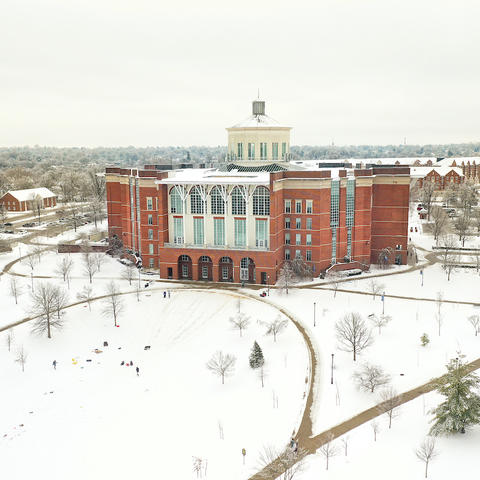 William T. Young Library with snow on the grounds and individuals sledding on the bowl in front.