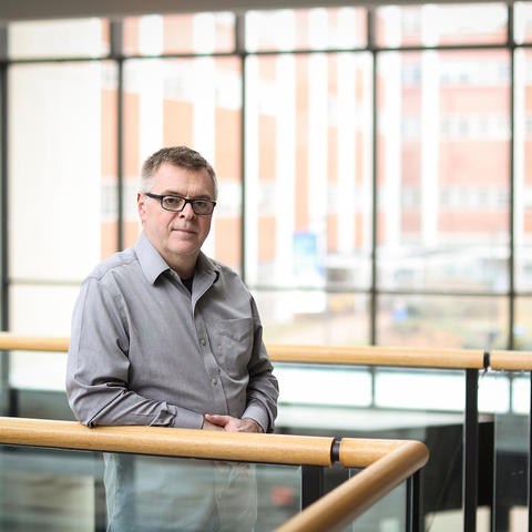 M. Paul Murphy leans against a railing inside a building in front of big windows