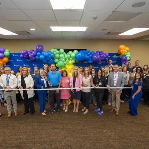 Group photo of ribbon cutting under colorful balloon arch