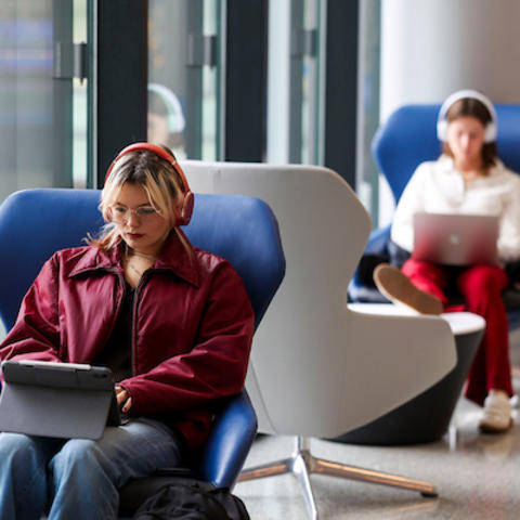 People seated in modern lounge chairs using tablets and laptops in a bright indoor space.