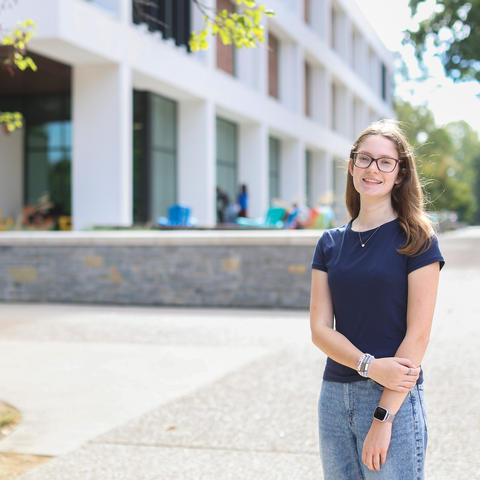 Person standing on a campus walkway in front of a modern academic building.